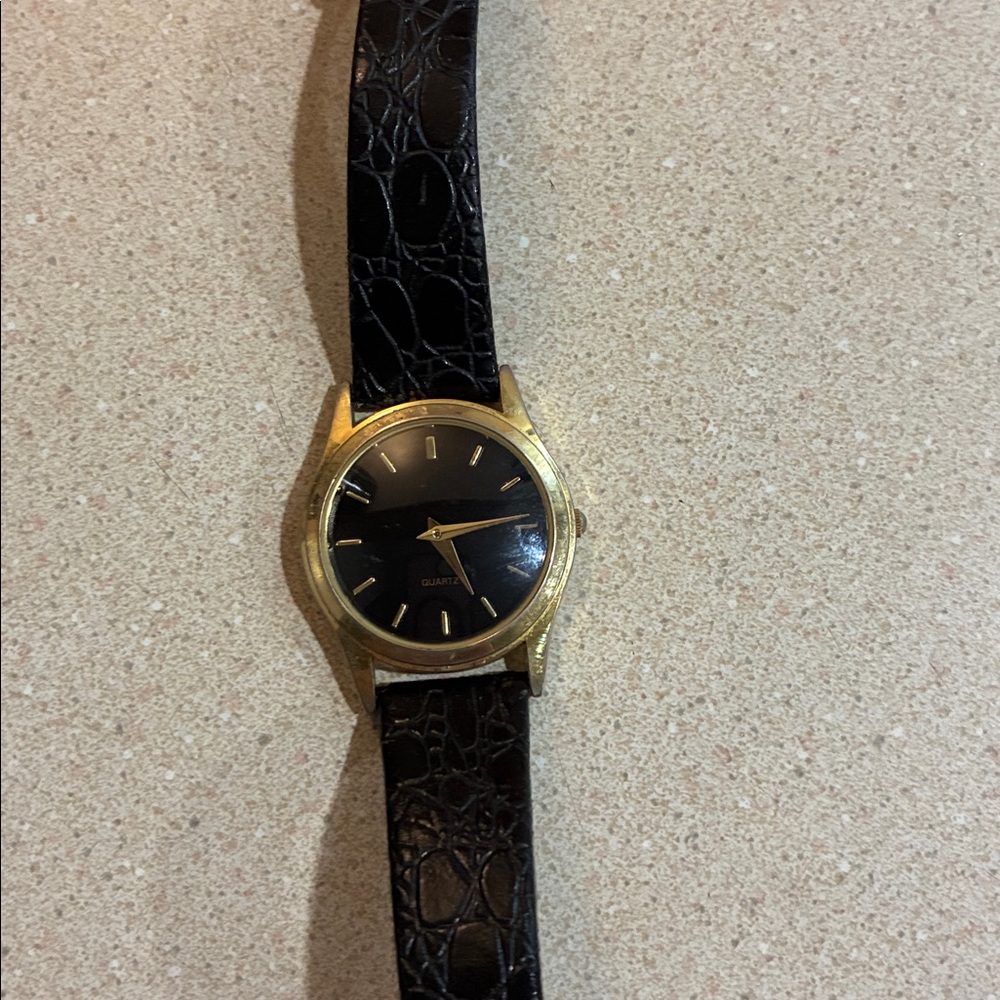 A Quartz Black and Gold Watch with Crocodile Pattern Strap. The strap is worn.